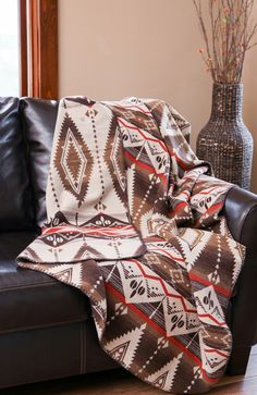 a brown and white blanket sitting on top of a black leather couch next to a vase