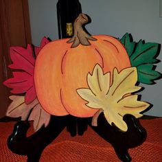 a painted pumpkin sitting on top of a wooden stand next to a bottle of wine