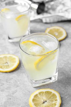 two glasses filled with lemonade sitting on top of a gray table next to sliced lemons