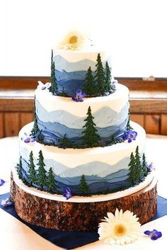 a three tiered cake with pine trees and flowers on the top is sitting on a table