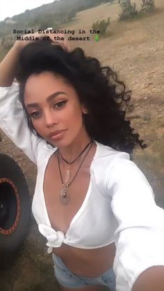 a woman posing in front of a tire with her hand on her head and wearing a white shirt