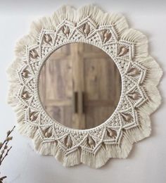 a white doily mirror hanging on the wall next to a vase with dried flowers