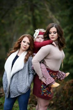 two women standing next to each other with one holding a baby and the other carrying another woman