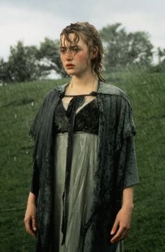 a woman standing in the rain wearing a long green dress and cape with her hands on her hips