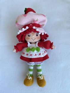 a crocheted doll is dressed in a red dress and hat with green trim