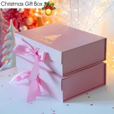 two pink boxes with bows are sitting on a table next to a christmas tree and decorations