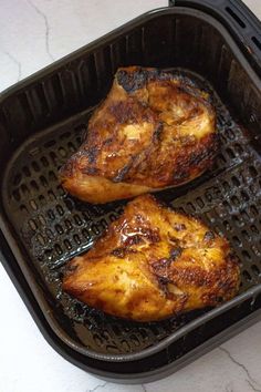 two pieces of chicken sitting on top of a black grill grates in a pan