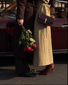 two people standing next to each other with flowers in their hands and one holding a purse