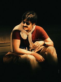 a man sitting on the ground wearing sunglasses and a scarf around his neck is looking at something in front of him