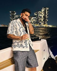 a man standing on the back of a boat talking on a cell phone while holding a drink in his hand