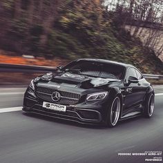 a black car driving down the road with trees in the backgroung area