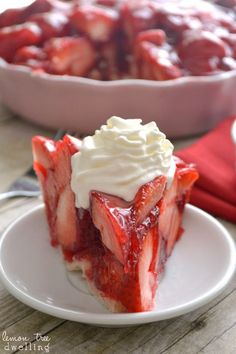 a white plate topped with a slice of cake covered in whipped cream and strawberries