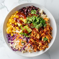 a white bowl filled with chicken, beans and coleslaw on top of a marble table