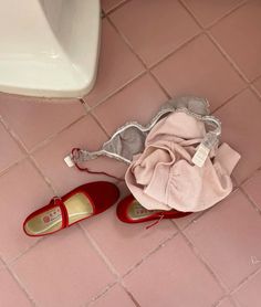 a pair of red shoes sitting on top of a pink tiled floor next to a white sink