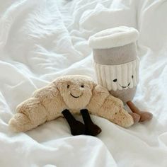 two stuffed animals laying on top of a bed next to a coffee cup and sock