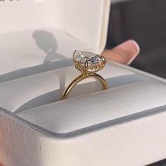 a woman's hand holding an engagement ring in a white box with gold accents