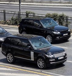 two black range rovers are driving down the street in front of each other,