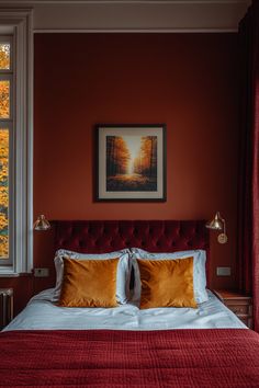 a bed with red sheets and pillows in front of a painting on the wall above it