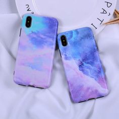 two phone cases are sitting on top of a white sheet with blue and purple clouds