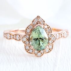 an engagement ring with a large green stone surrounded by small white diamonds in rose gold