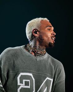 a man with white hair and piercings on his neck wearing a gray sweater in front of a black background