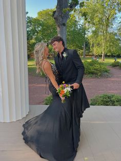 a man and woman dressed in formal wear standing next to each other on a porch