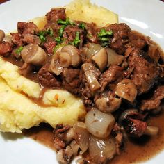 a white plate topped with mashed potatoes and meat covered in mushroom gravy