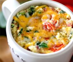 a close up of a cup of food with broccoli and tomatoes in the background