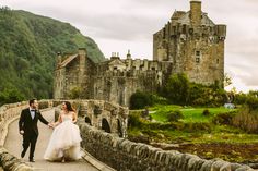 a bride and groom walking on a bridge in front of a castle