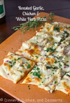 a pizza with chicken and white herb toppings on a cutting board next to a bottle of beer