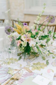 an arrangement of flowers on a table with place cards and wine glasses in front of it