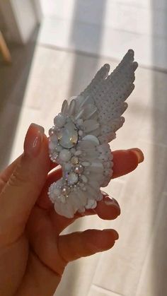 a hand holding a white brooch with pearls on it's back and wings