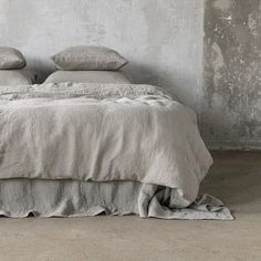 an unmade bed with two pillows on top of it in a room that has concrete walls