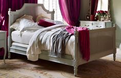 a white bed with purple drapes and pink pillows on it's headboard