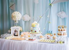 a table topped with lots of cakes and cupcakes next to a wall covered in clouds