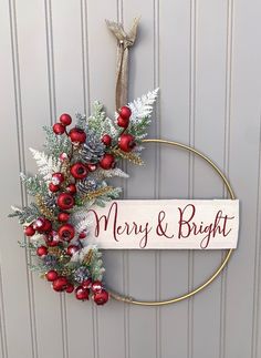 a merry and bright christmas wreath hanging on the front door with red berries, pine cones and evergreens