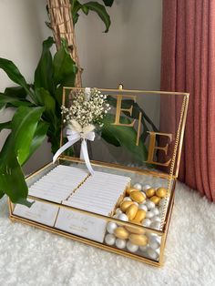 a gold box filled with lots of candies next to a potted plant on top of a white rug