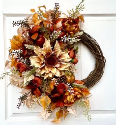 a wreath is hanging on the door with flowers and leaves around it in front of a white door