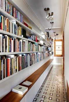 a long bookshelf filled with lots of books next to a wall full of books