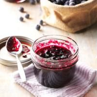 blueberry sauce in a glass jar and spoon on a napkin next to some berries