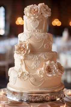 a three tiered wedding cake with roses on top and candles around the edges, sitting on a table