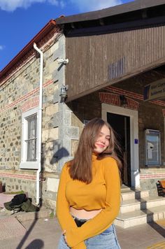 a woman standing in front of a stone building with her arms crossed and looking at the camera