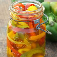 a jar filled with pickles sitting on top of a wooden table next to green peppers