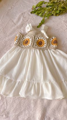 a white dress with sunflowers is laying on a bed next to some flowers