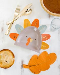 a turkey shaped paper plate next to a pie and silverware on a white table