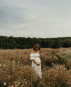 a pregnant woman standing in a field holding her belly and looking off to the side