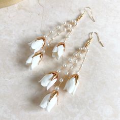 three pairs of earrings with white flowers and pearls hanging from them on a marble surface