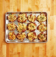 a metal pan filled with mini pizzas on top of a wooden table next to a knife