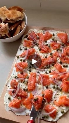 a pizza sitting on top of a wooden cutting board next to a bowl of chips