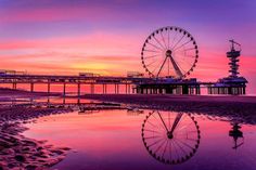 a ferris wheel sitting on top of a sandy beach next to the ocean at sunset